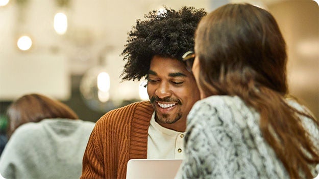 Two people indoors sitting one in front of the other. One person is smiling.