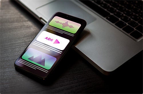 A phone placed on a laptop displays the word "ads" and other images on its screen.