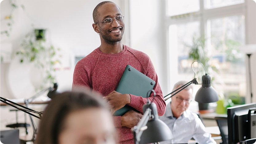 A person standing holding a closed laptop and smiling.